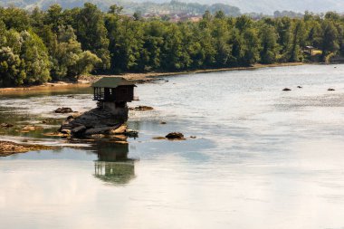 Small wooden cabin on a rock in the middle of river Drina, Serbia. clipart