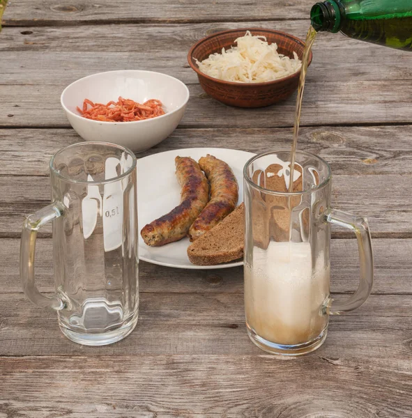 Glasses for beer on a background of sausages of a grill and smoked squid on a table