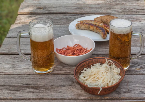 Glasses for beer on a background of sausages of a grill and smoked squid on a table