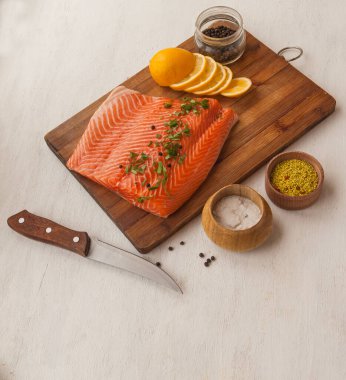 Kırmızı balık ve limon filetosu, baharatlı kavanozların yanındaki kesim tahtasının üzerinde.