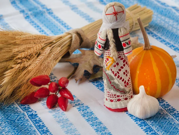 Folk motanka doll, a sheaf of grain, pepper and pumpkin on the embroidered tablecloth (mass produced products). Concept of harvest