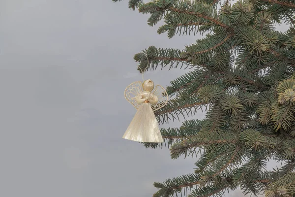 空の背景に青いトウヒの枝にぶら下がっているわら天使 コンセプト冬のキリスト教の休日 量産製品 — ストック写真