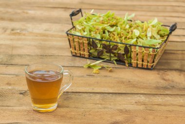 Ahşap bir masada ıhlamur çiçeği ve şeffaf bir kupa limon çayı.