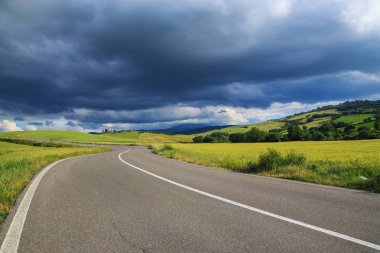 Curvy asphalt road in Tuscany and dramatic clouds sky. Italy clipart