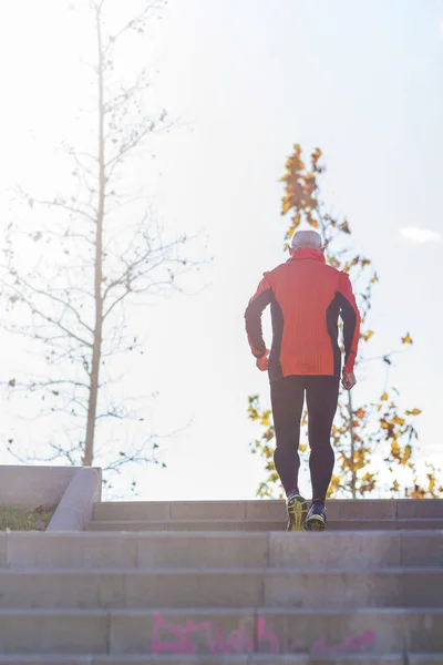 Vista trasera de un atleta caucásico mayor entrenando corriendo por las escaleras al aire libre en un parque en un día soleado —  Fotos de Stock
