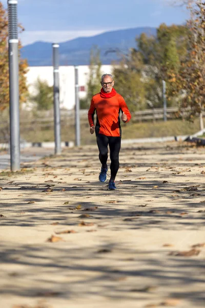 Vista frontal de un hombre mayor en ropa deportiva corriendo en un parque de la ciudad en un día soleado —  Fotos de Stock