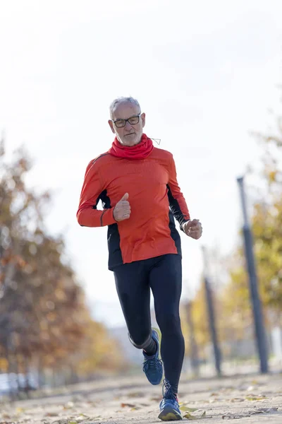 Frontansicht eines älteren Mannes in Sportkleidung beim Joggen in einem Stadtpark an einem sonnigen Tag — Stockfoto