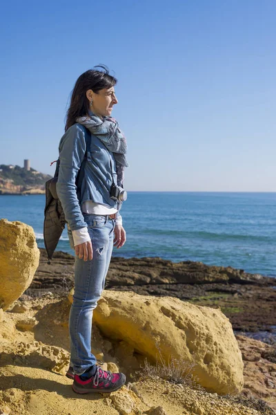 Vista lateral de uma jovem sonhadora vestindo roupas casuais em pé na praia enquanto olha para o horizonte em um dia brilhante — Fotografia de Stock