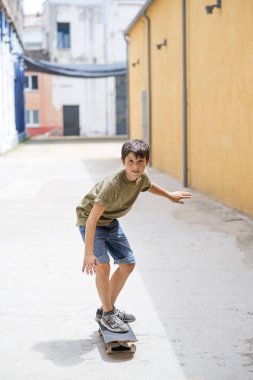Güneşli bir günde sokakta sürme neşeli bir patenci çocuğun ön görünümü