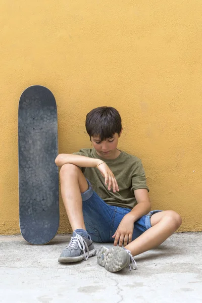 Vista frontal de um menino sentado no chão apoiado em uma parede amarela enquanto olha para baixo — Fotografia de Stock