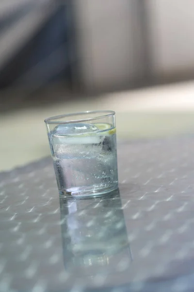 Glass of water with ice on a metallic table outdoors in a sunny day
