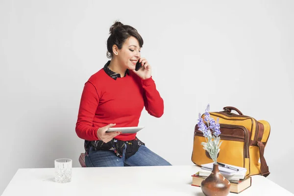Вид спереди красивой женщины с пончиком, сидящей на табуретке, пользуясь телефоном и держа планшетный компьютер на белом фоне — стоковое фото