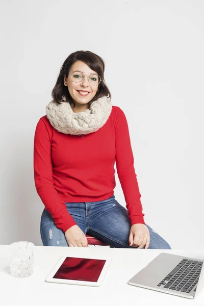 Front view of a beautiful woman in casual wear sitting on a stool while looking camera against white background — Stock Photo, Image