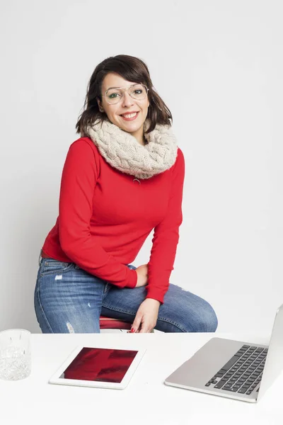 Front view of a beautiful woman in casual wear sitting on a stool while looking camera against white background — Stock Photo, Image