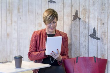 Bir kafede tablet kullanarak kırmızı ceketli kadın