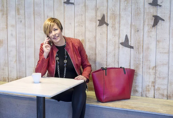 Vacker blond kvinna pratar på mobiltelefon när du sitter i ett kafé — Stockfoto