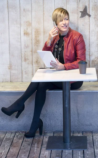 Красивая блондинка разговаривает по мобильному телефону, сидя в кафе — стоковое фото