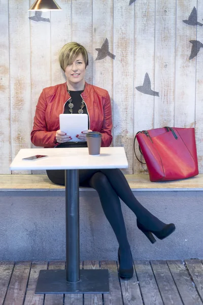 Mulher em um casaco vermelho usando tablet em um café — Fotografia de Stock