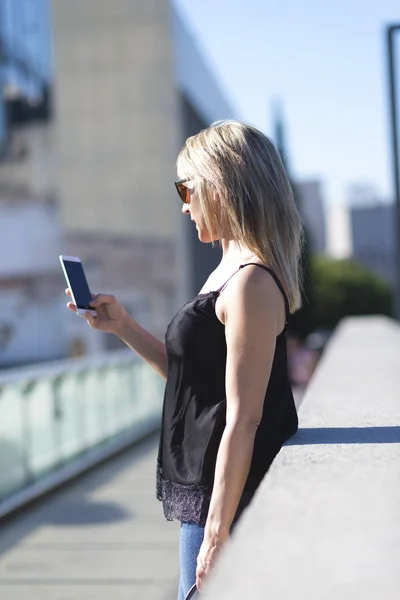 Vista lateral de una chica revisando un teléfono inteligente en la calle — Foto de Stock