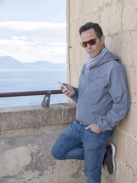 Akıllı telefonunu kullanırken terasta duran güneş gözlüğü takan genç adam. — Stok fotoğraf