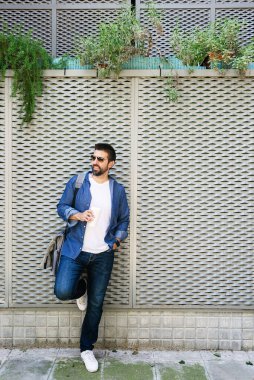 Mavi tişörtlü yakışıklı bir adamın portresi. Elinde kahveyle metalik bir arka planda duruyor.