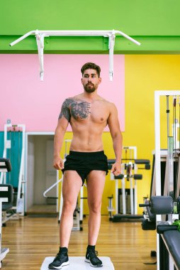 Yakışıklı, seksi, üstsüz, üstsüz, spor salonunda dikilip yan yan bakan adam.