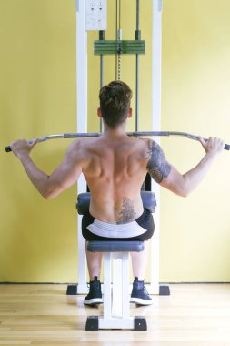 Sağlık kulübünde sıhhatli bir adam var. Ağırlık İndirme Makinesi üzerinde çalış