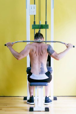 Sağlık kulübünde sıhhatli bir adam var. Ağırlık İndirme Makinesi üzerinde çalış