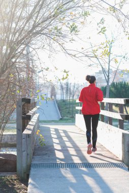 Güneşli bir günde şehir parkında koşan genç bir kadın.