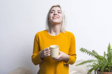 Elinde kahve fincanı tutan mutlu kadın yukarı bakıyor. Neşeli tavrı bitkilerin zenginleştiği huzurlu bir ortamda bir anlık rahatlama izlenimi veriyor..