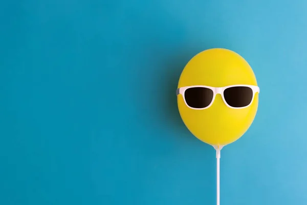 Yellow party balloon with sunglasses on a blue background