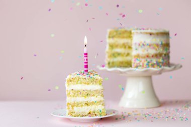 Funfetti 'nin doğum günü pastası. Bir mum ve pembe arka planda tek bir dilim kesilmiş.