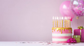 Růžový narozeninový dort se zlatými svíčkami a balónky