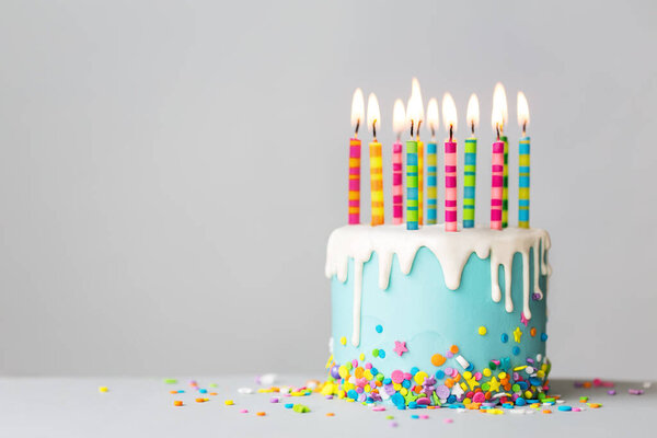 Торт на день рождения с белой капельной глазурью, брызгами и красочными праздничными свечами
