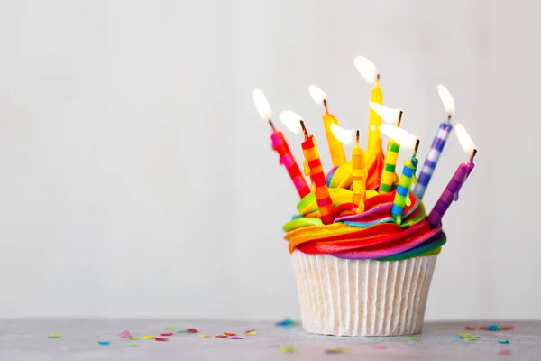 虹の霜降りとカラフルな誕生日キャンドル付きの誕生日カップケーキ — ストック写真