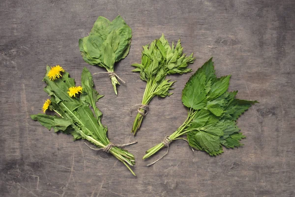 Bunches of spring edible wild herbs (slightly dried): nettle, dandelion, goutweed, plantain. On rustic wooden background.