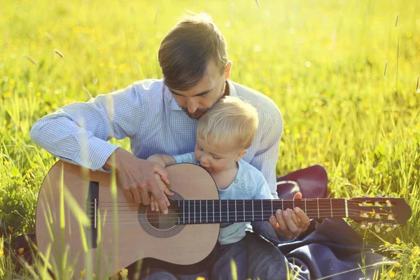 Father teaches his son to play guitar on summer meadow. Time together dad and son outdoor.