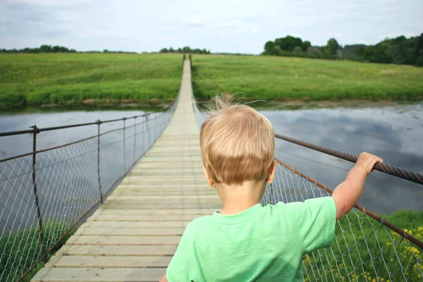 Cute toddler boy overcoming fear, prepering to crossing suspension bridge. Face your fears, look into the future, opening a new way concept.