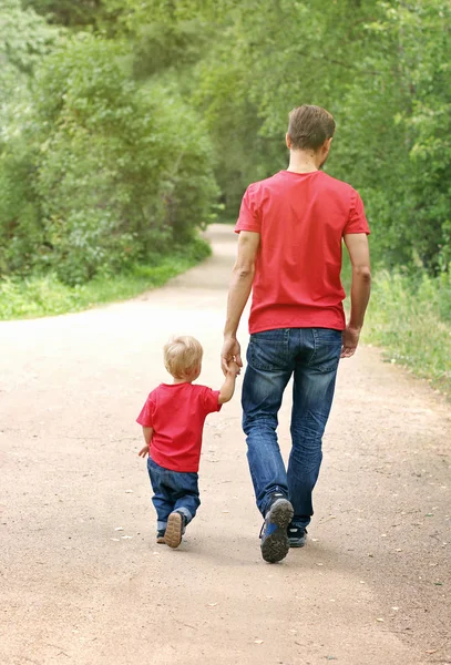 Baba ve yürümeye başlayan çocuk parkta elele yürüyor. Babalık kavramı. Aile göz giyim.