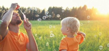 Şirin bebek sarışın çocuk ve babası sabun köpüğü ile yaz sahada oynuyor. Güzel gün batımı ışık. Otantik yaşam tarzı görüntü.