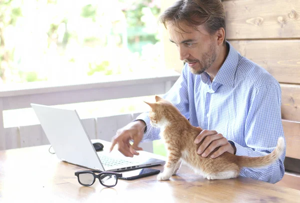 Genç işadamı dizüstü bilgisayarda onun kedi ile açık bir teras üzerinde çalışıyor. Serbest veya ev ofis kavramı.
