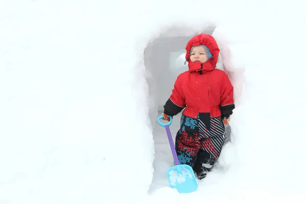 シャベルとかわいい男の子は 大きな雪の吹きだまりの雪の洞窟を掘っていきます 冬の楽しみの概念 コピー スペース — ストック写真