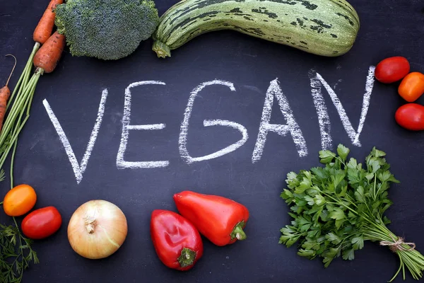 Inscription VEGAN on chalk board, surrounded by different fresh vegetables. Healthy food lifestyle.