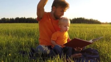 Baba ve sevimli yürümeye başlayan çocuk oğlu yaz alan birlikte kitap okumak. Ebeveynlik kavramı. Canlı kamera, ağır çekim.