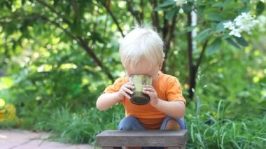 Şirin yürümeye başlayan çocuk içecekler taze yeşil smoothie cam açık. Sağlıklı gıda veya vegan kavramı.