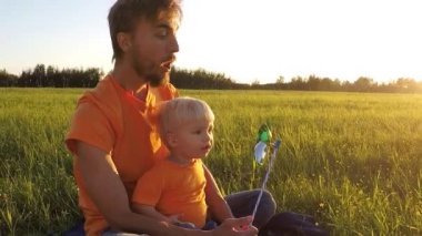 Baba ve yürümeye başlayan çocuk oğlu ile fırıldak günbatımı üzerinde oynamak. Canlı kamera, ağır çekim.