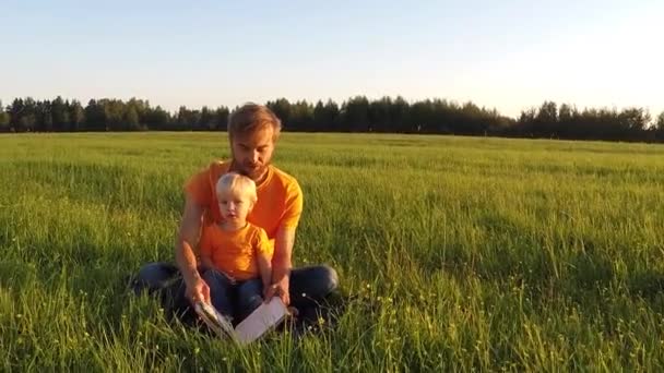 父と息子のかわいい夏の畑で一緒に本を読む感情的に ライブ カメラ スローモーションでズーム — ストック動画