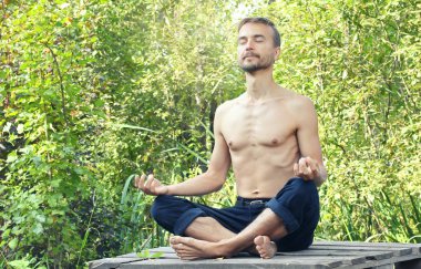 Genç poz lotus ile gözleri kapalı ve meditasyon oturan adam sakallı. Yeşil orman arka plan üzerinde. Yoga doğa kavramı. 