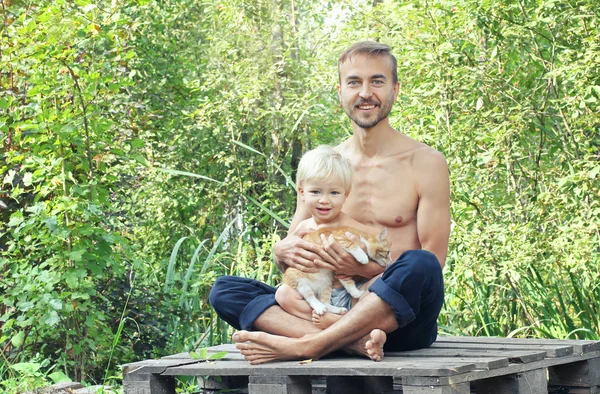 Father, son and kitten sitting together on nature. They look at camera and smile. Happy family concept.