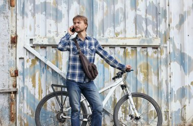 Sakallı hippi adam bisiklet ve deri çanta ile görüşmeler Smartphone grunge şehir duvar arka planı. Modern kent yaşam tarzı kavramı. 